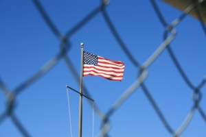 American flag behind a chain link fence. (Image: via Shutterstock)